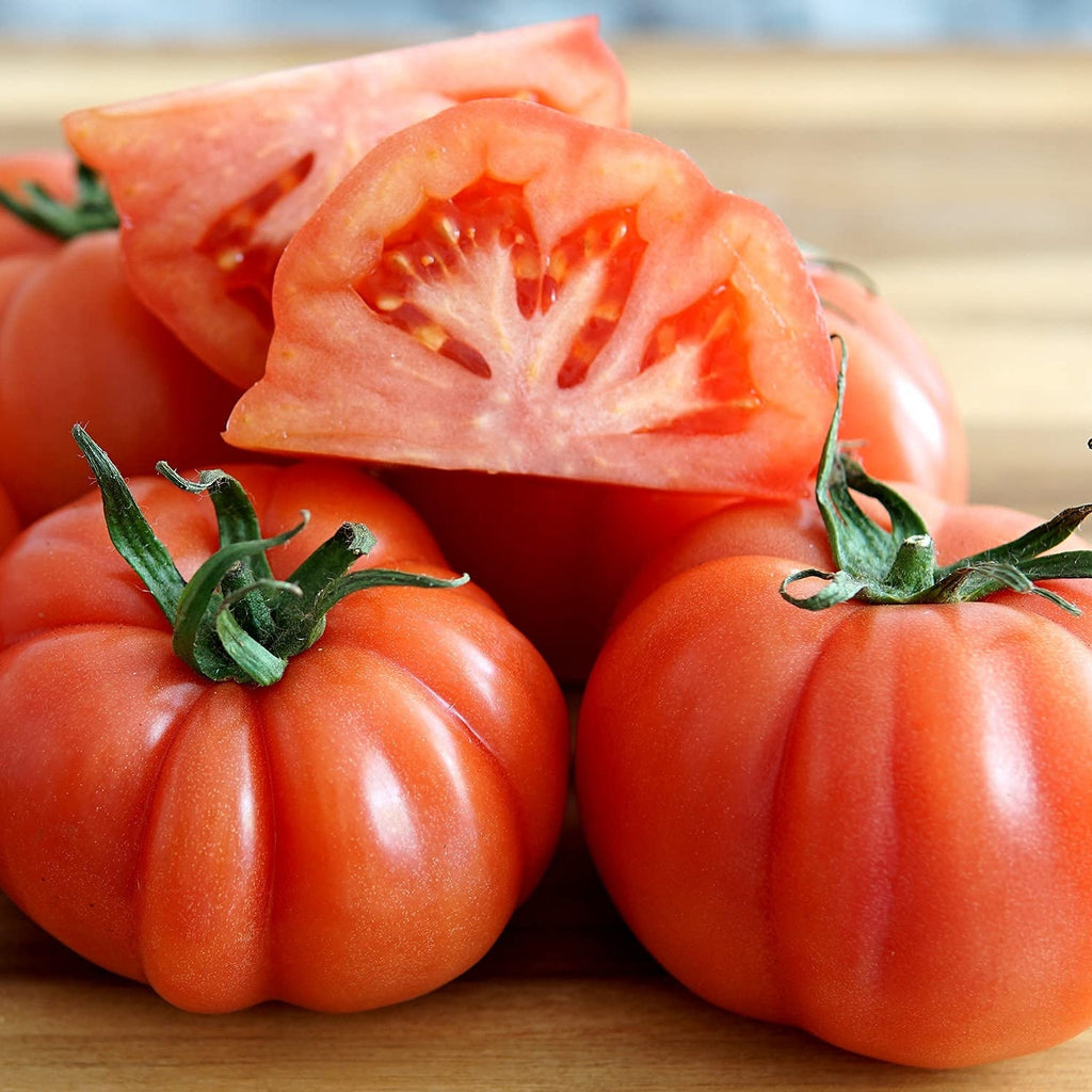 Свежие помидоры сорта Costoluto Fiorentino, целые и нарезанные, на деревянной поверхности